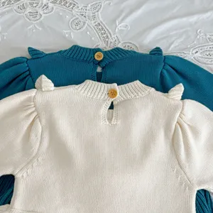 Close-up detail of knitted baby romper with puff sleeves and back button closure.
