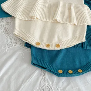 Detailed view of the knitted baby romper with lovely ruffles and cute wooden button accents.