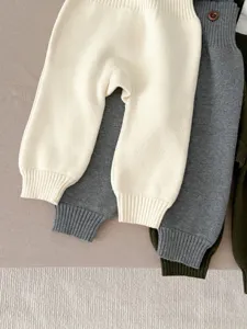 Close-up detail showing the soft knit texture and ribbed cuffs of baby trousers in multiple colors.