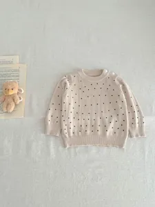 Infant baby knit sweater detail view, beige color with black polka dots, soft fabric texture.