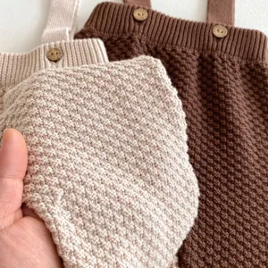 Vista dettagliata della tutina in maglia per neonato con morbida trama e bottoni di legno.
