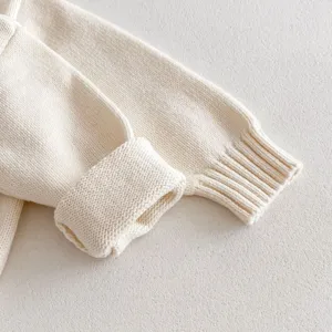 Close-up detail of infant knit sweater sleeve, soft ribbed cuff, neutral background texture.