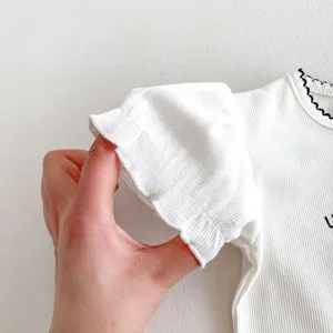 Primo piano sulla manica di una maglietta bianca a costine da neonato con bordo nero.