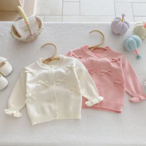 Detail view of baby girl knit cardigan with cute bows, soft fabric and delicate buttons.