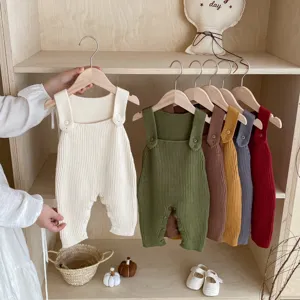 Detailed view of baby knit strap rompers in various colors hanging neatly on wooden racks.