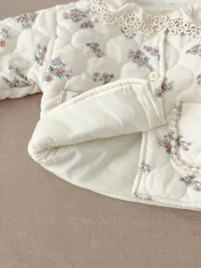 Close-up detail of winter baby girl quilted floral jacket with delicate lace collar.
