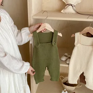 Detailed view of knitted baby strap rompers hanging on a wooden rack in warm lifestyle tone.