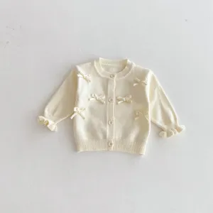 Close-up detail of infant knitted cardigan featuring cute bows and sweet ruffled cuffs.