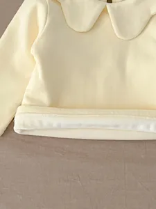 Close up detail of baby girl yellow top peter pan collar soft fabric garment texture display