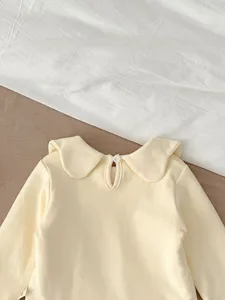 Close-up detail of cute baby girl long sleeve top in soft yellow with sweet peter pan collar.