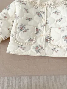 Close-up detail of infant floral quilted jacket featuring delicate lace collar and pockets.