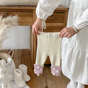 Detail von Babystrickleggings, gemütlicher Ton mit süßen Bommel-Bündchen, weiche Winter-Babyhose.