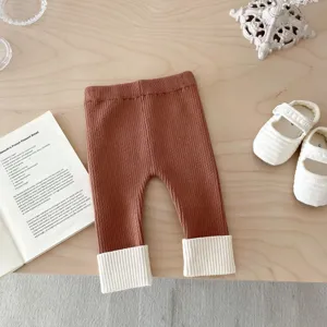 Dettaglio leggings in maglia per neonati, pantaloni marroni con risvolti bianchi.