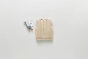 Detail view of beige quilted kids vest flat lay with wooden giraffe toy on pure white background.
