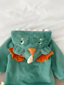 Vista dettagliata della tutina in peluche verde da neonato a tema dinosauro con corna arancioni.