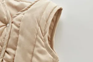 Close-up detail view of kids khaki quilted vest showing shoulder cut and snap buttons.