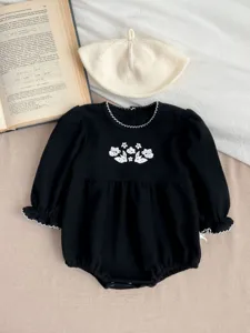 Detailed closeup of black baby romper with white floral embroidery and cute scalloped collar.