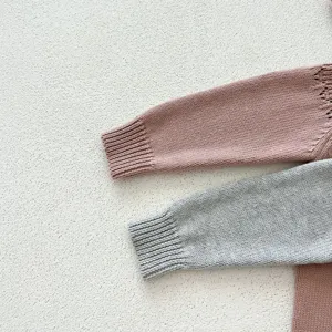 Detalle en primer plano de mangas de mameluco de punto para bebé con textura rosa y gris.