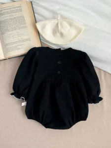 Detailed view of black baby romper featuring white lace trim, long sleeves and beret prop.