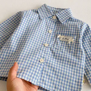 Vista dettagliata della camicia per bambini a quadri blu con taschino e decorazioni.