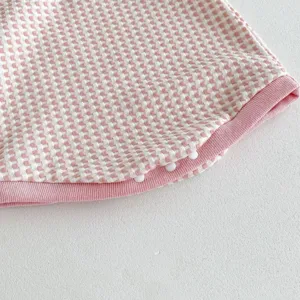 Pink and white checkered baby clothing detail showing soft waffle fabric and snap buttons.