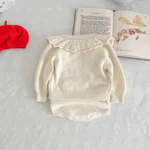 Close-up detail of infant knitwear set, cream white cotton yarn with delicate ruffle collar.