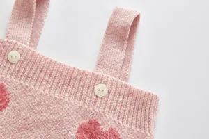 Baby pink knit romper detail showing cute fuzzy heart pattern and white buttons closeup.