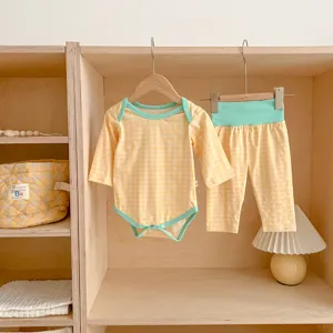 Set tutina e pantaloni a quadri gialli da neonato su scaffale in legno con lampada carina.