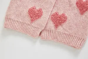 Detail view of pink knitted baby cardigan featuring fluffy heart patterns and ribbed hem.