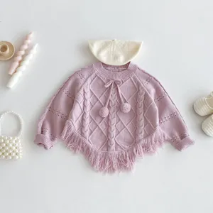 Detailed view of baby girl knitted poncho sweater with fringe, pom-poms and jacquard design.