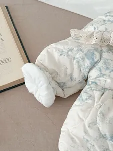 Detail view of baby quilted winter jumpsuit featuring delicate lace ruffle collar and cozy plush cuffs.