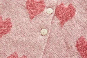 Detailed shot of infant pink knit cardigan with fuzzy heart pattern and white buttons.