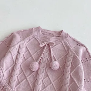 Pink knit sweater detail featuring cable pattern, pom-poms, and cute fringe hem design.