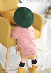 Detail van gebreid baby-meisjesvest, roze wollen trui met pompons en schattige baret.
