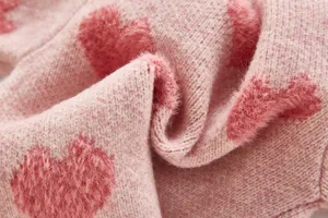 Close-up of soft pink knit fabric featuring cute fuzzy heart patterns for baby clothing details.