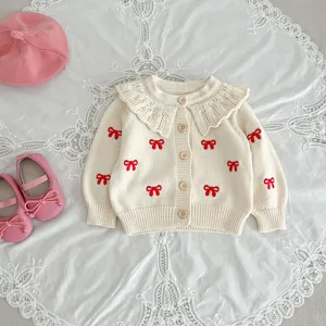 Baby girl knit cardigan detail, cute red bows and lace collar on beige wool fabric.
