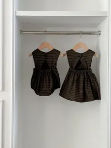 Detail shot of matching baby girls plaid sleeveless romper and dress hanging inside closet.