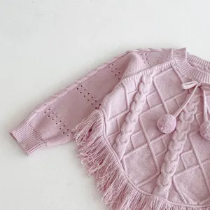 Girls pink knit sweater detail showing cable pattern, tassels and cute pom-poms close up.