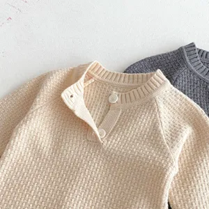 Close-up detail of infant knit romper, ribbed neckline with buttons, soft textured fabric.