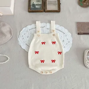 Infant knit romper detail, beige cotton fabric with cute red bow embroidery and wooden buttons.