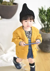 Details van handgemaakt baby gebreid vest met pompons in het geel, gezellige herfst trui.
