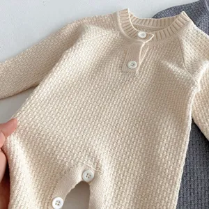 Close-up detail of beige knitted baby romper with raglan sleeves and cute buttons.