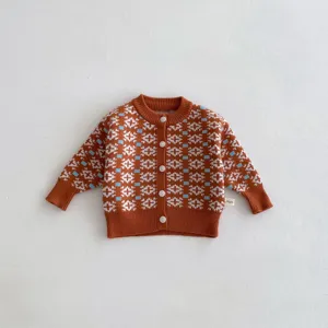 Infant knitted cardigan close-up, caramel color with geometric pattern and white buttons, cozy fabric detail.