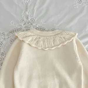 Infant knitted cardigan close-up showing delicate lace collar and soft cream textured fabric.