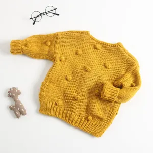 Gedetailleerd uitzicht van handgemaakte baby trui in gele gebreide stof met leuke pompons.