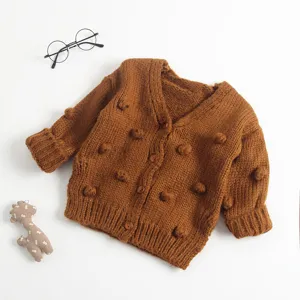 Gedetailleerd overzicht van bruin gebreid babyvest met handgemaakte pompons voor de herfst.