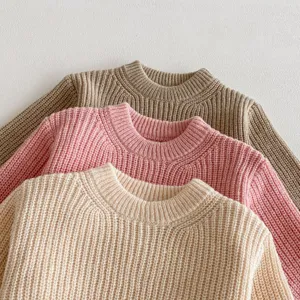 Detalle de suaves jerséis de punto para bebé apilados en encantadores colores sólidos.
