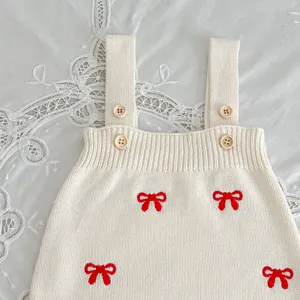 Close-up detail of infant knit romper with red bow embroidery and small wood buttons.