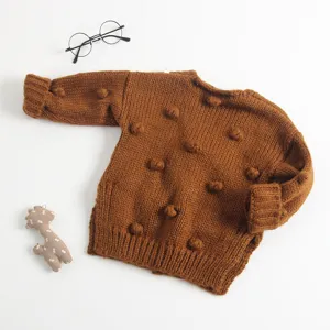 Detailopname van het bruine gebreide babyvest met zachte handgemaakte pompons en textuur.