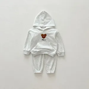 Infant cotton hooded tracksuit detail showing embroidered bear motif and soft grey fabric.